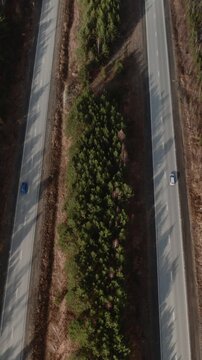 Top down drone footage of a two lane highway cutting through dense pine forest with a few cars, rural landscape in the Ural Mountains, Russia, travel and transport concept