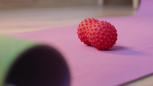 Hand placing red spiky massage ball onto fitness mat close up