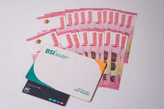 Makassar, Indonesia, September 20, A Bank Syariah Indonesia savings book and a debit card placed over a fanned-out arrangement of Indonesian 100.000 rupiah banknotes.
