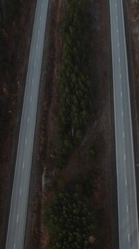 Top down drone footage of a two lane highway cutting through dense conifer forest with a single car driving along the road in the Ural region, Russia