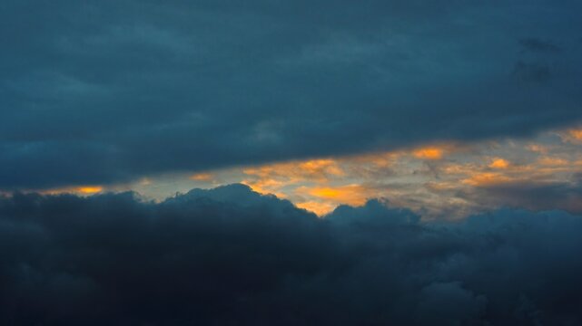 Dramatic sunset sky background with dark stormy clouds and orange light breaking through. Moody cinematic atmospheric backdrop.