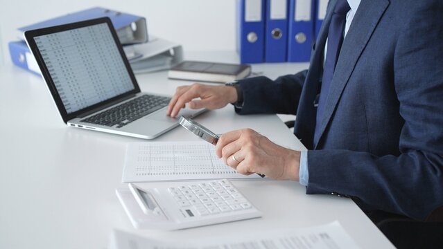 Professional auditor analyzing financial data, scrutinizing numbers and documents with a magnifying glass, performing detailed accounting and business analytics in an office setting