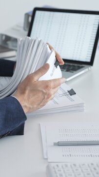 Accountant reviewing financial reports and organizing documents, managing business data and preparing paperwork for auditing and tax preparation at an office desk