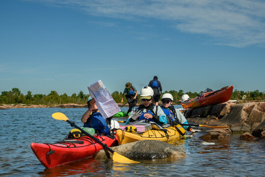 Sea kayak group reorganizing navigation charts beside a small rock outcrop during a break, blue sky copy space and room for text, Georgian Bay, Ontario