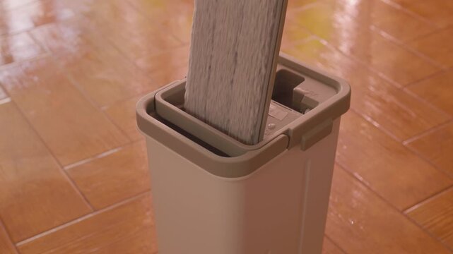 Domestic mop wringing sequence over dual compartment gray bin on glossy terracotta floor midlate