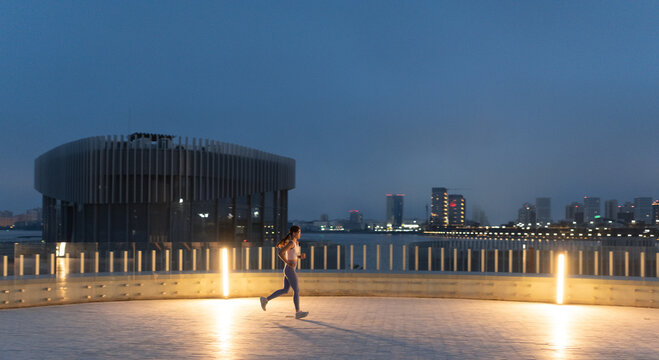 Sportswoman exercises at urban riverside with downtown in background.