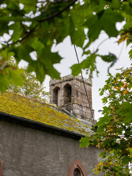 27th September 2026, Embleton, Cumbria. Saint Cuthberts Church, a historic stone structure, stands under a cloudy sky, partially obscured by autumnal foliage, evoking a sense of timeless tranquility.