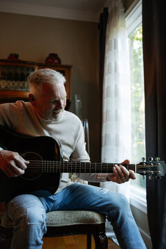 Older man playing acoustic guitar by window, candid moment