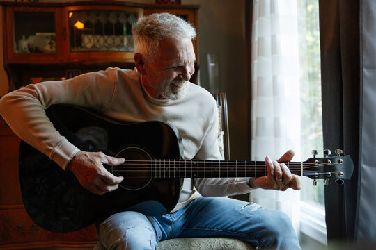 Senior man playing acoustic guitar at home, smiling in candid mo