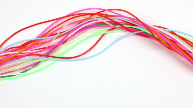A tangle of multicolored threads moves, forming waves against a white background.
