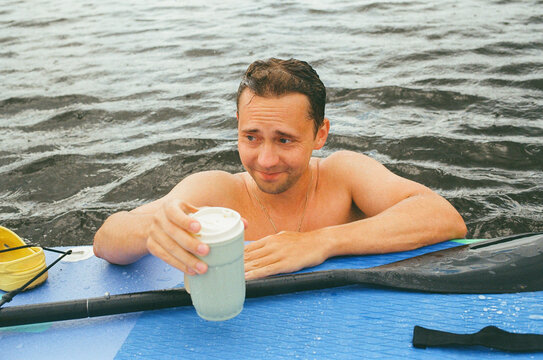 Man on Paddleboard Holding Drink in Water