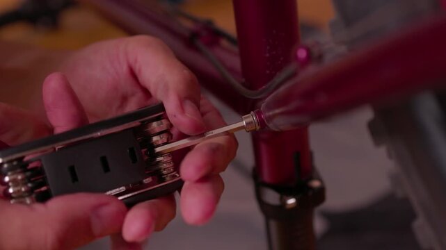hands adjusting bicycle seat post clamp in indoor workshop setting with red and black components focused and practical close-up perspective on metallic and plastic materials.