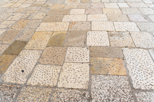 Old limestone street paving with square slabs in cream, ochre and grey tones, pitted chiselled surfaces and worn joints seen in perspective, concept of historic Mediterranean streets and natural ston