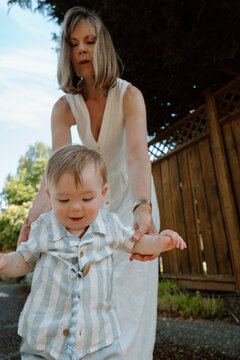 Grandmother helping toddler take first steps outdoors, candid mo