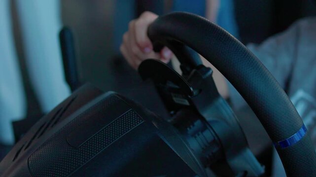 focused adult driving simulation setup in indoor gaming environment with steering wheel and pedals over the shoulder view in black and red plastic and metal materials.