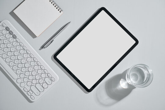 Minimalist workspace with tablet, keyboard, and water glass on white