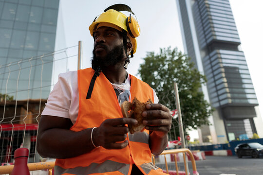 Construction worker taking break eating sandwich on urban site