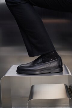 Man wearing black shoes and black socks on metal stool