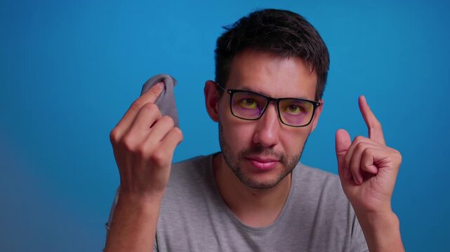 Man cleaning glasses with a cloth, in blue background, with glasses, cloth, with glass, textile texture, from a frontal perspective, with blue, gray accents, and neutral mood.