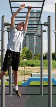Teenage boy moves across monkey bars at outdoor fitness playground. He trains upper body strength, balance and coordination during recreational workout. Active lifestyle and fitness