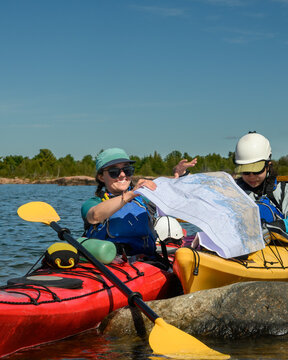 Smiling kayaker and partner unfolding a nautical chart during a sea kayaking course, vertical sky copy space and room for text, Georgian Bay, Ontario