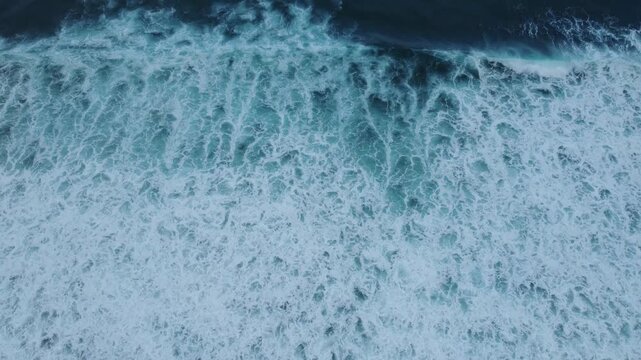 Abstract close-up aerial view of blue ocean waves and seafoam moving across the surface, offering a calm yet energetic coastal nature background without visible shoreline.