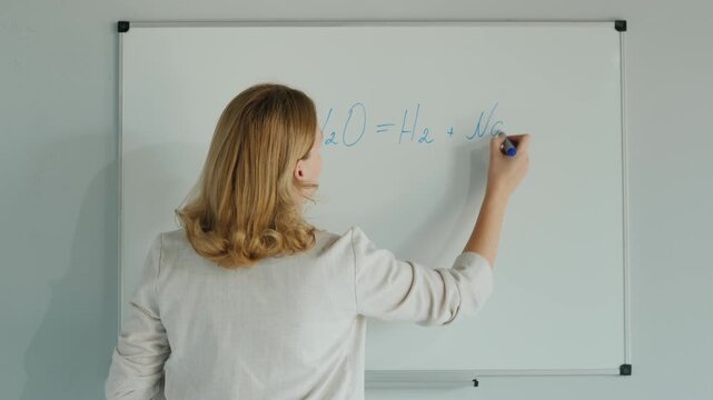 Teacher writes chemical equation for reaction of sodium with water on a whiteboard.