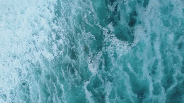 Turquoise seawater and rolling surf waves collide and spread into frothy whitewater, filmed from above as a peaceful natural seascape background.