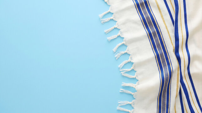 Top view of traditional Jewish tallit prayer shawl with blue and gold stripes on light blue background with copy space.