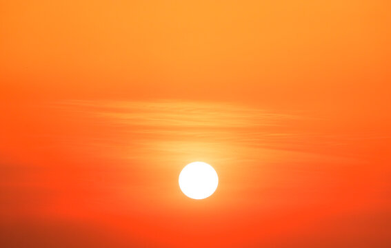 Bright big sun rising in vibrant orange morning sky with soft clouds, hot summer sunrise or sunset background with copy space.