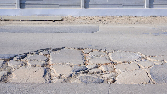 Large cracked and damaged concrete road with potholes needing repair, dangerous asphalt street surface infrastructure problem.