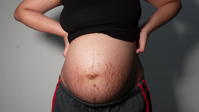 Pregnant woman standing and holding her lower back, expressing tiredness and physical discomfort commonly associated with the later stages of pregnancy.