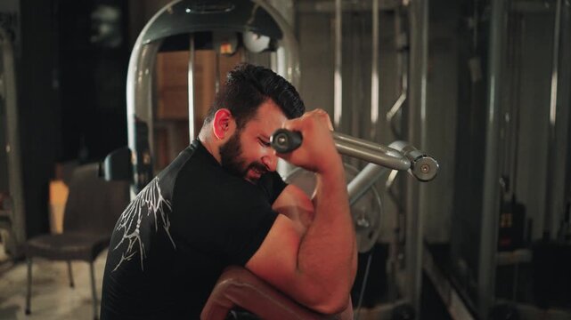 Muscular male athlete executing machine bicep curls on a preacher bench focusing on arm hypertrophy and physical fitness inside a health club.