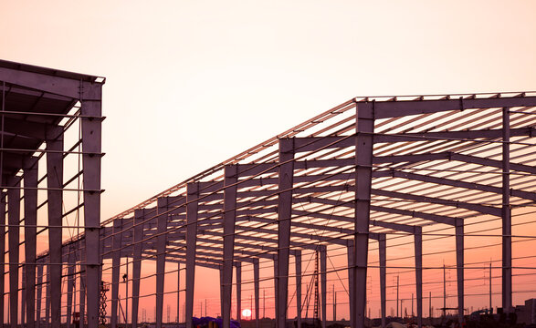 Silhouette metal framework of industrial warehouse buildings structure in factory construction site against sunset sky background 