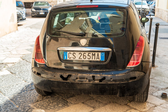 Bari, Italy - Aug 4, 2026: Rear of an old black Lancia Ypsilon with a damaged scratched bumper and Italian number plate parked on a cobbled street beside bollards