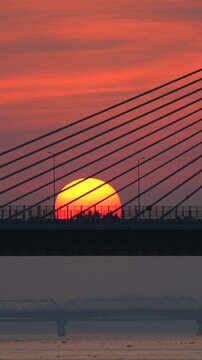 The setting sun appears beneath the cables of a Bridge