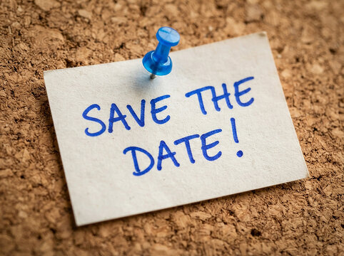 Save the date text written on a white paper note pinned to a brown cork bulletin board