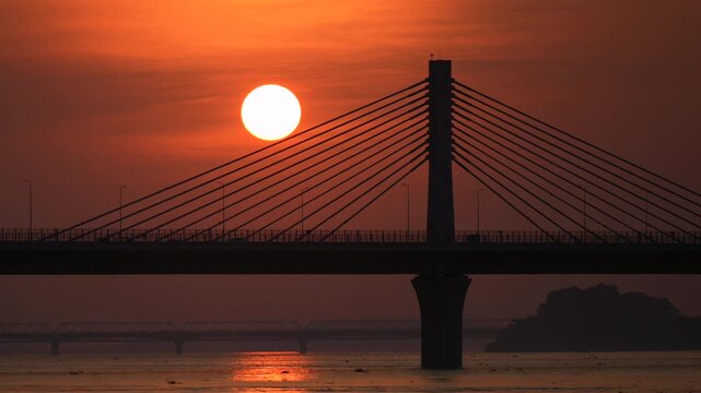 The setting sun appears beneath the cables of a Bridge