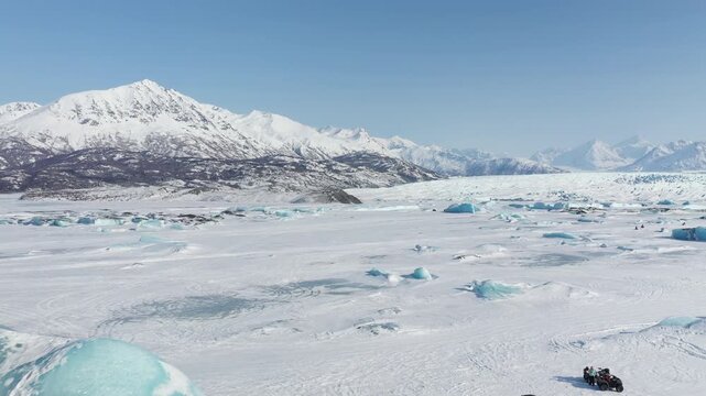 Wide Aerial View Over Glacial Snowfield with Blue Ice and Mountain Peaks