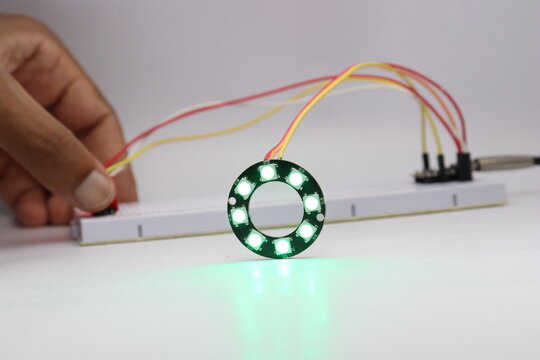 ARGB LED ring light glowing in color controlled by a sensor and microcontroller in the background