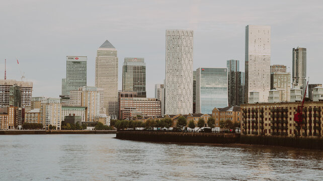Panoramic view of Canary Wharf skyline with HSBC tower and modern office buildings along River Thames in London on cloudy day