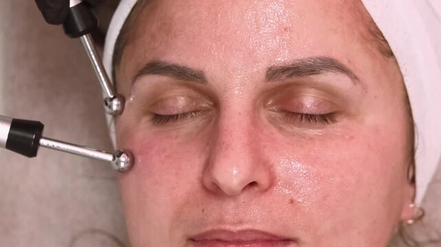 Microcurrent facial. Woman treatment. Cosmetologist hands in black gloves using professional device for lifting skin procedure.