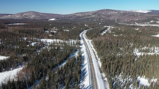 Aerial View Following Car Driving Along Snow-Covered Highway Through Forest
