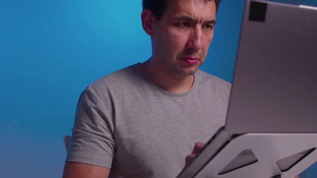 Close-up right hand adjusting tilted laptop mounted on adjustable metal hinge bracket with visible cables, reflecting soft light on aluminum housing in indoor workspace
