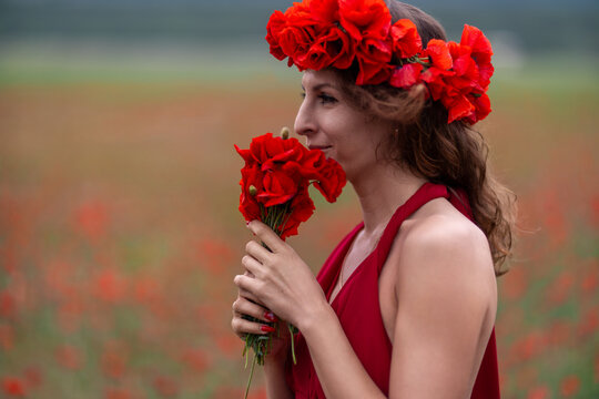 Woman poppy field holding flowers wearing red crown in beautiful summer landscape