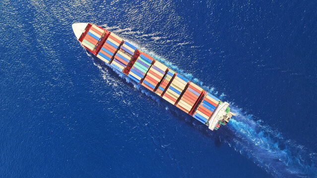 Aerial drone drone point of view photo above huge fully loaded container ship with colorful containers overlooking deep blue sea near logistics port
