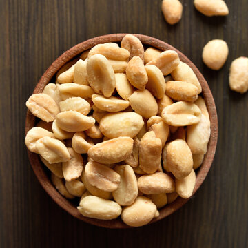 Salted roasted peanuts in bowl on brown wooden background
