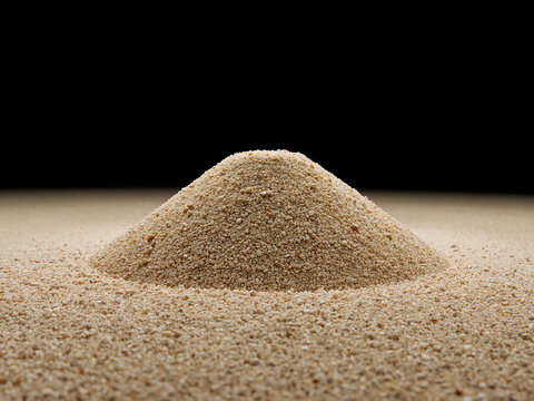 A perfectly shaped conical pile of fine beige sand resting on a flat surface against a dark black background, macro of texture