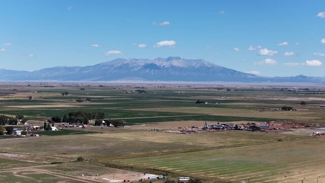 Aerial of agricultural fields and farm buildings in the San Luis Valley near La Jara Colorado with the Sangre de Cristo mountain range in the background under a blue sky