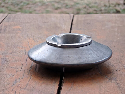 Plain metal ashtray resting on a weathered wooden table outdoors